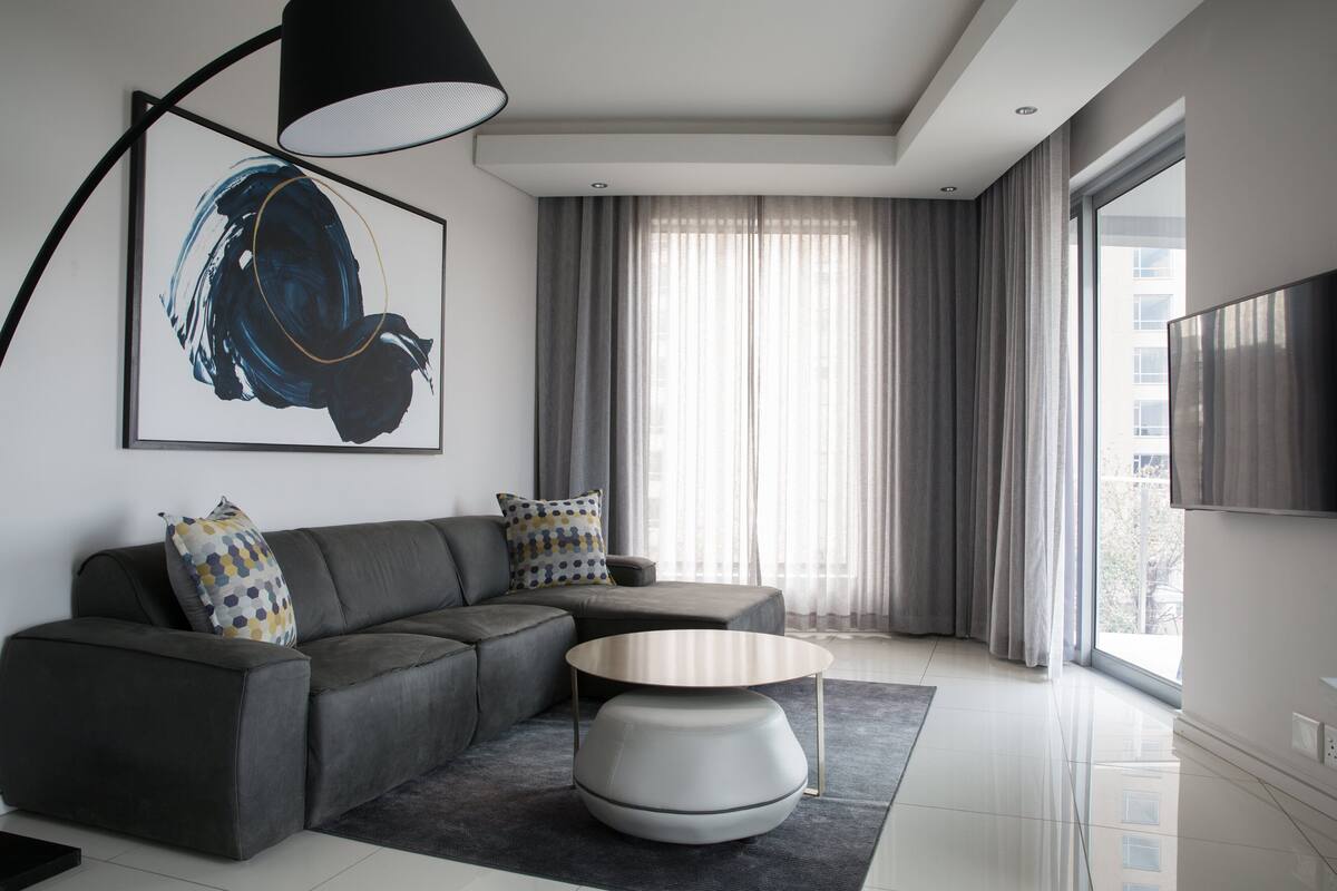 Una sala de estar moderna con un sofá gris, una mesa de centro redonda y un cuadro abstracto grande.