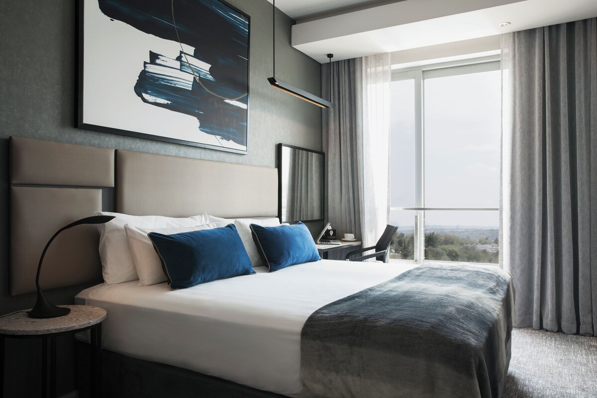 Een moderne hotelkamer met een groot bed, een bureau en uitzicht op de stad.