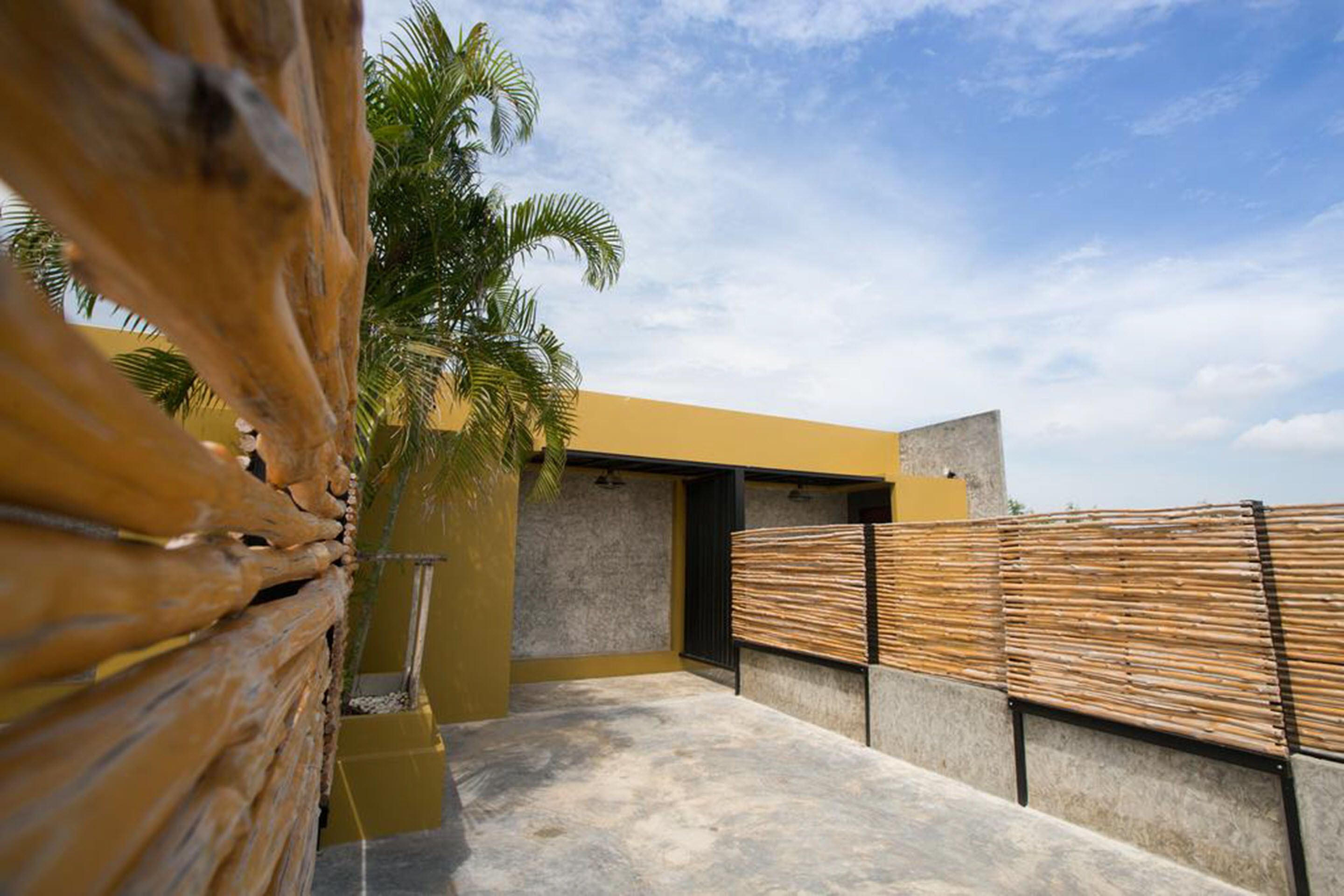 A modern outdoor space with a concrete floor, a yellow wall, and a bamboo fence.