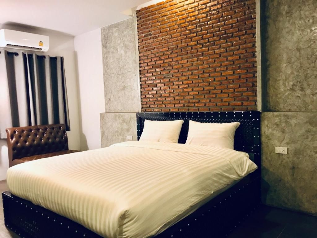 A bed with a headboard against a brick wall, a window with curtains, and a wall-mounted air conditioner.