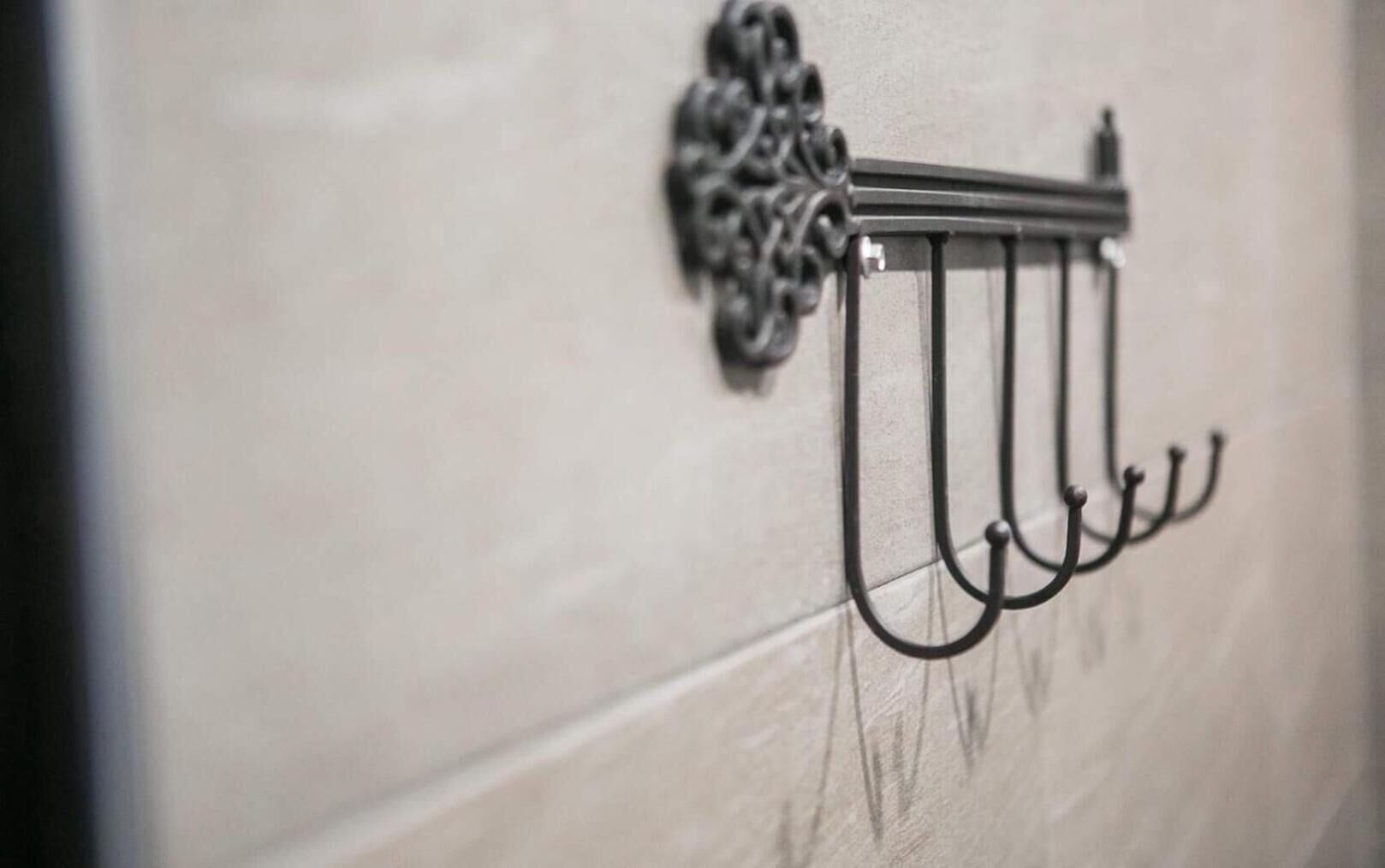 A metal hook with a decorative finial on a light-colored wall.