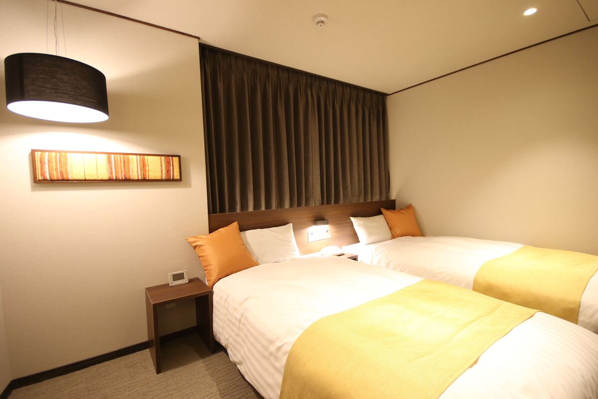 Una habitación de hotel con dos camas, una mesita de noche, una lámpara y un cuadro en la pared.