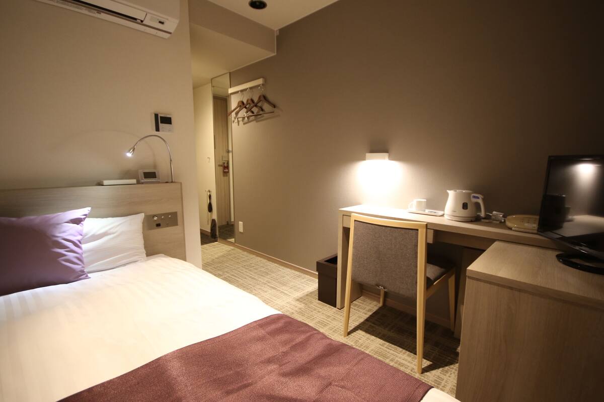 Habitación de hotel con cama, escritorio con computadora, cafetera y televisión.
