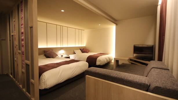 Quarto de hotel com duas camas, televisão e área de estar.