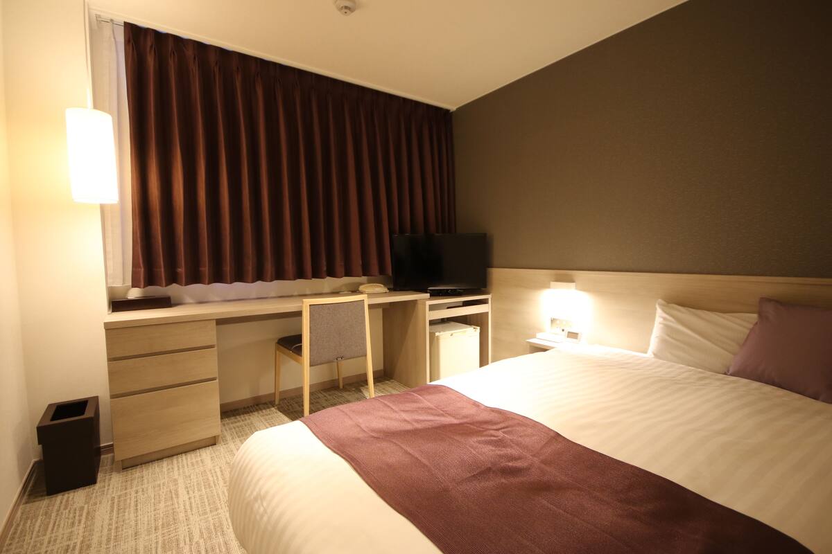 Una habitación de hotel con cama, escritorio con televisor, silla y lámpara.