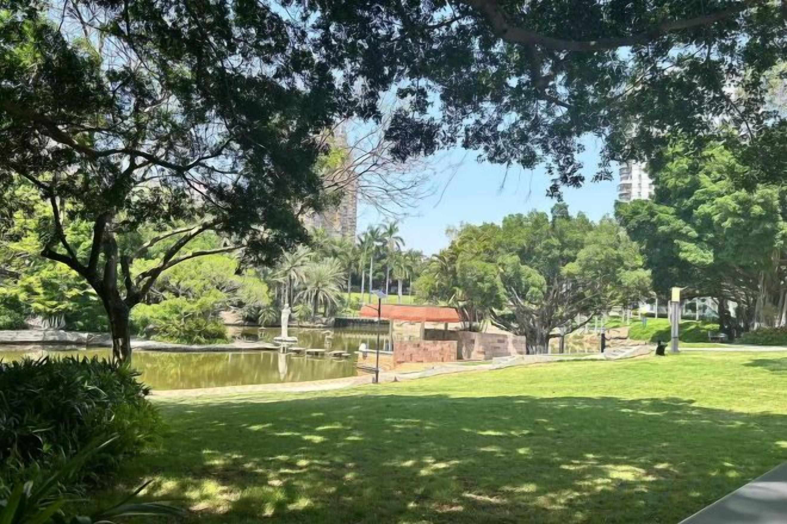A park with a pond, trees, and a building in the background.