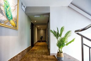 Um corredor com piso de madeira, um vaso com planta, uma obra de arte emoldurada e uma escada.