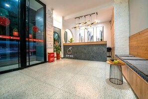 A hotel reception area with a glass door, a reception desk, and a seating area with a wooden bench. - Jiacheng Hotel (Xiamen Lianhua) (Xiamen)