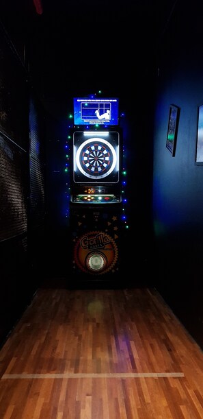Eine Dartscheibe mit digitaler Anzeigetafel und Dartmaschine, vor einer dunklen Wand mit Holzboden.