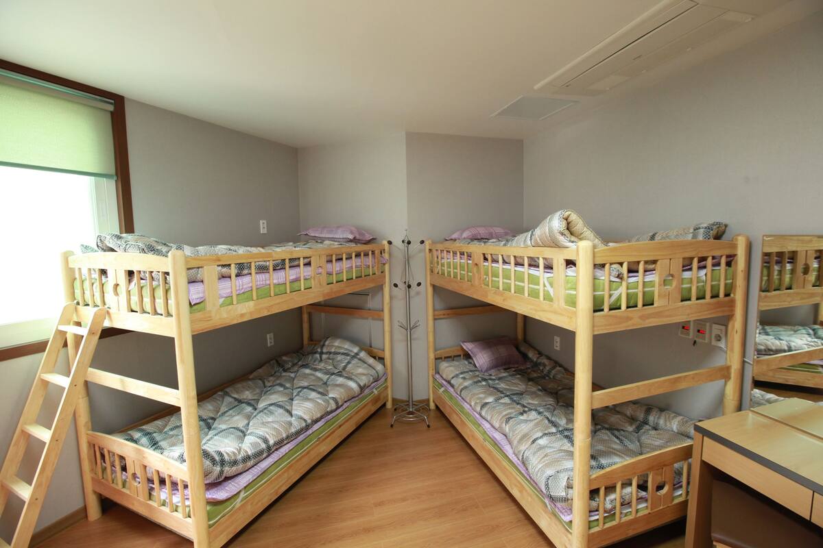 A room with four bunk beds, a desk, and a floor lamp.