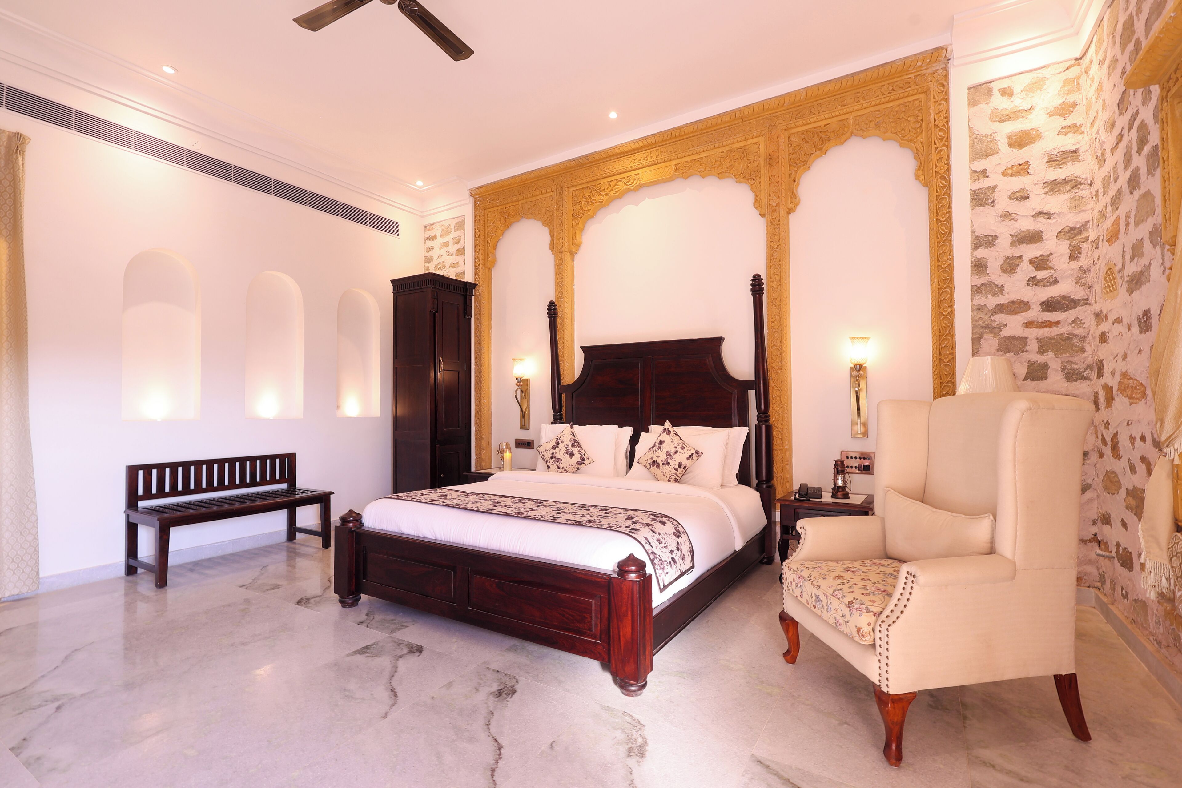 A bedroom with a four-poster bed, a bench, a sofa, and a chandelier.