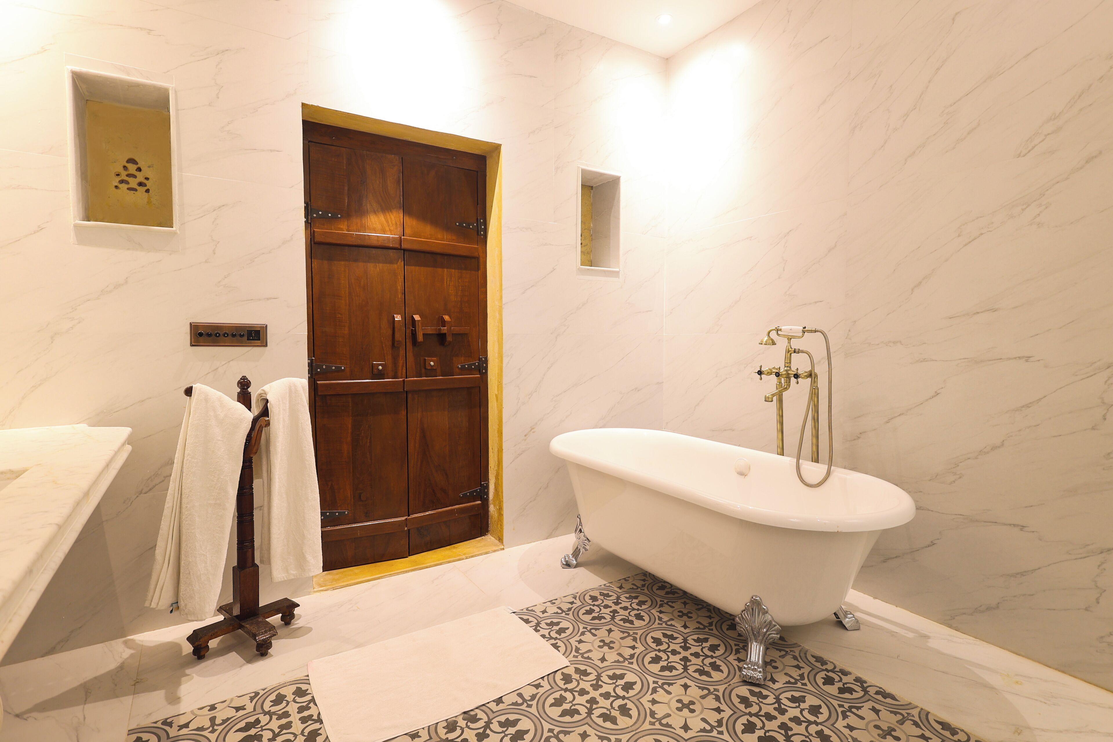 Une salle de bain avec une porte en bois, une baignoire sur pieds, un carrelage imitant le marbre et un lavabo blanc.