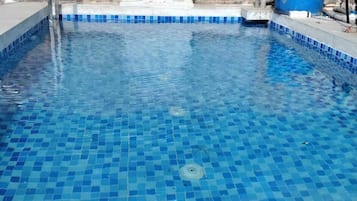 A swimming pool with blue mosaic tiles and a decorative stone headpiece on the wall.