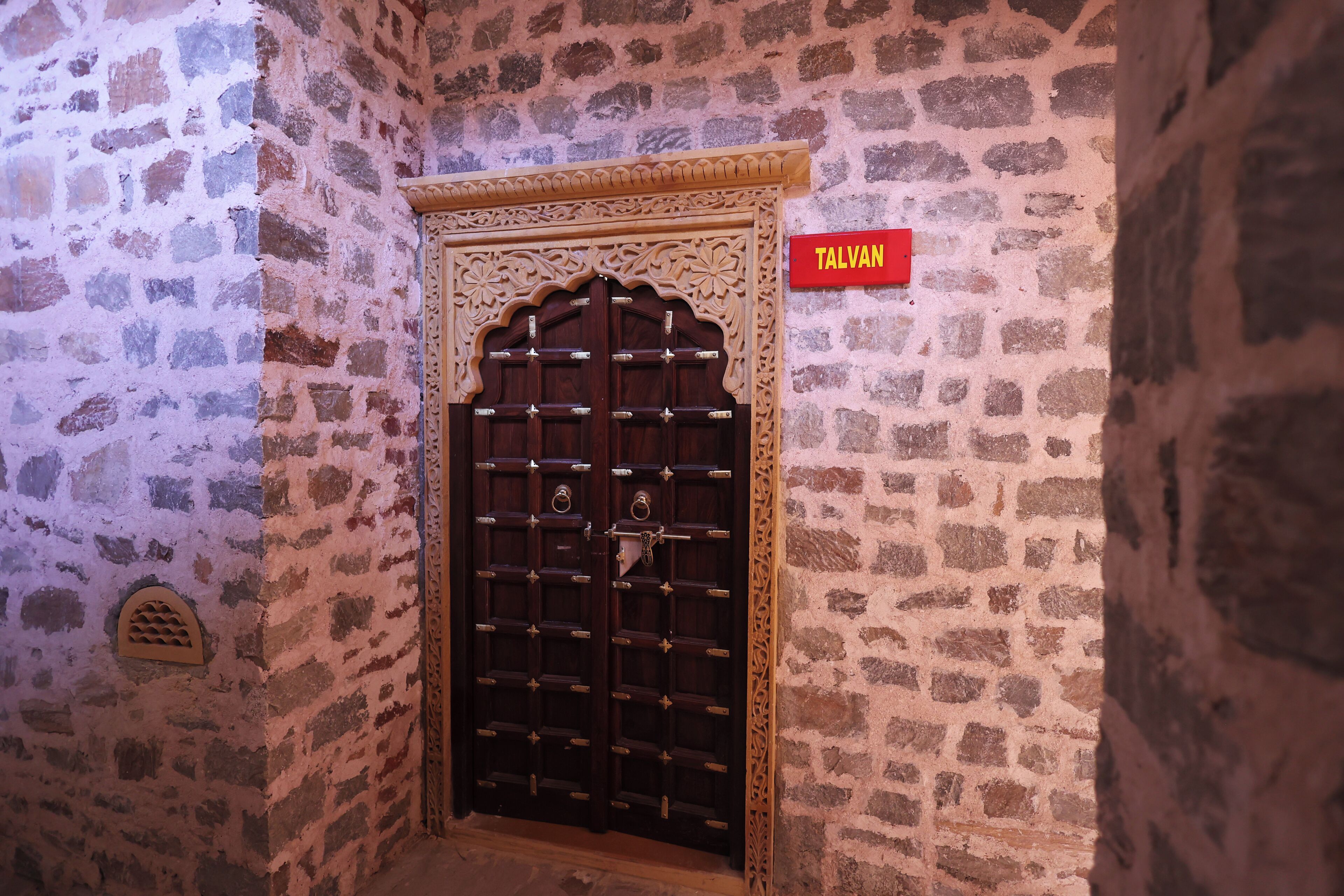 A stone wall with a wooden door and a red sign reading "TALVAN".