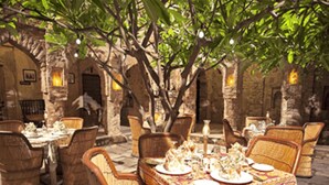 An outdoor dining area with wicker chairs and tables, stone walls, and hanging lights. - Fort Dadhikar, Alwar (Alwar)