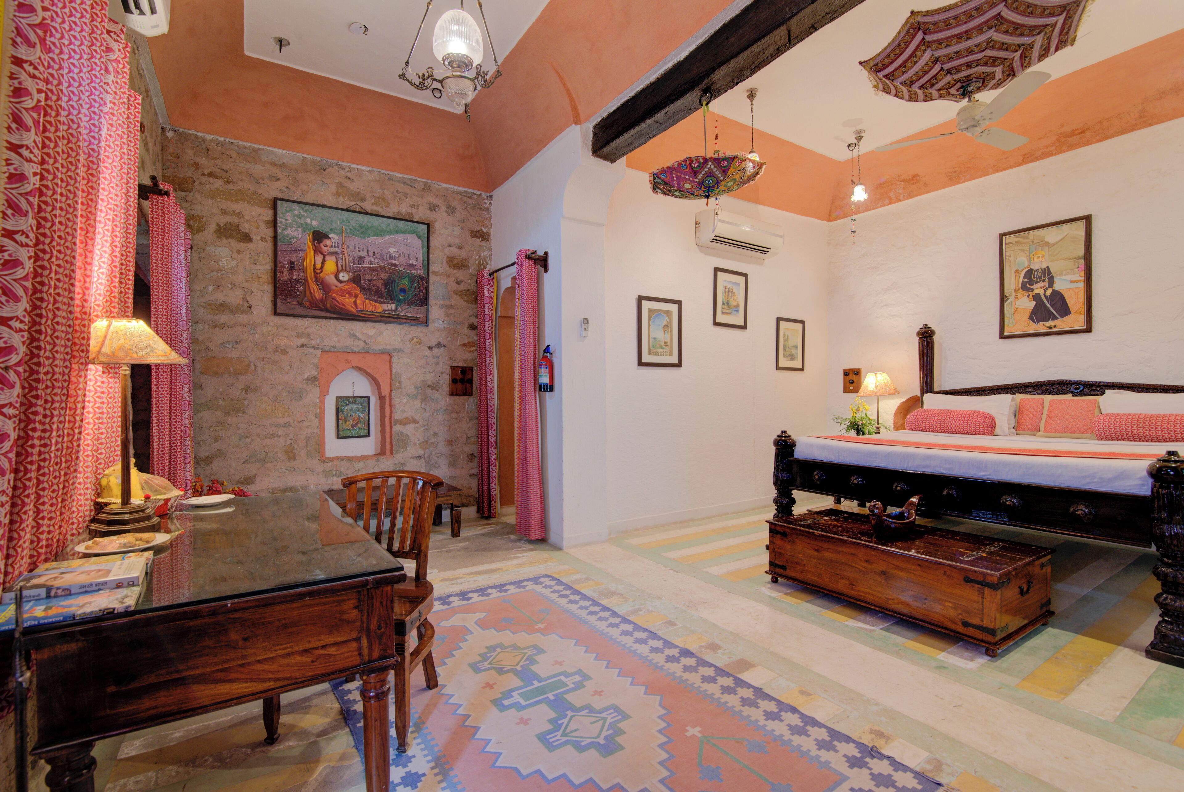 A cozy room with a wooden table, chairs, a bed with a patterned bedspread, and a colorful rug.
