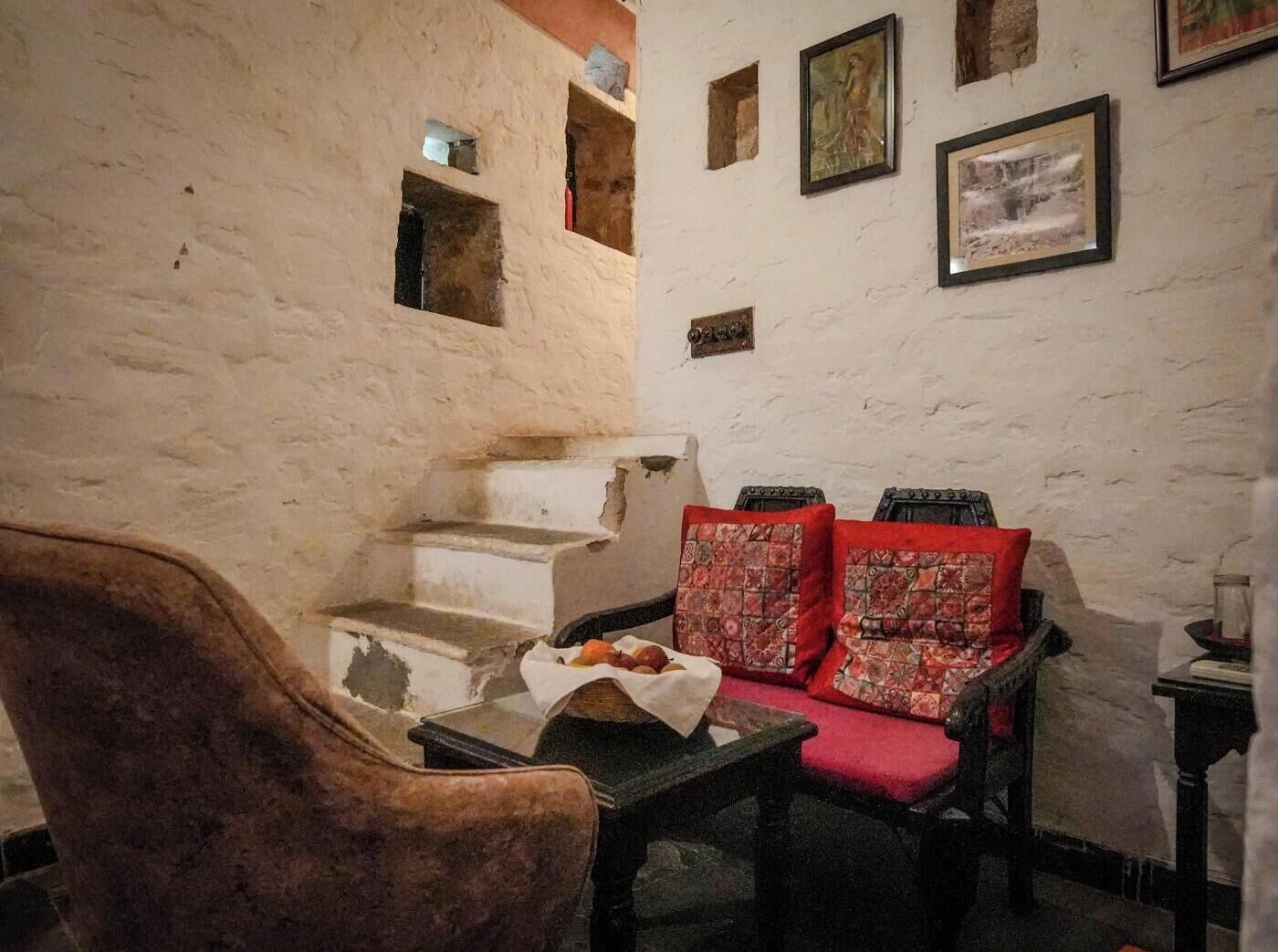 Un intérieur rustique avec un mur en pierre, une chaise en bois, une petite table avec un panier et un canapé agrémenté de coussins à motifs.