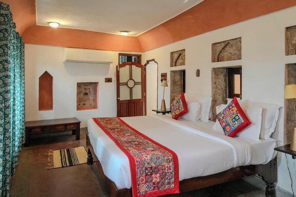 A bedroom with a large bed, a wooden nightstand, a desk, and a chair.
