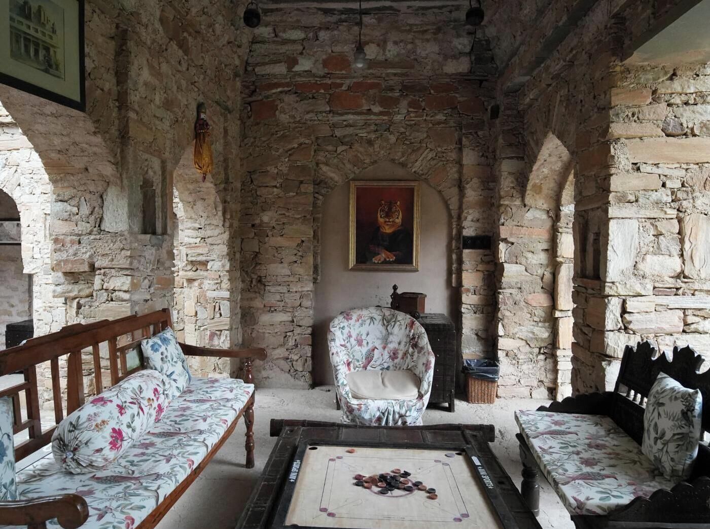 A rustic stone-walled room with two wooden sofas, a floral armchair, and a table with a board game.
