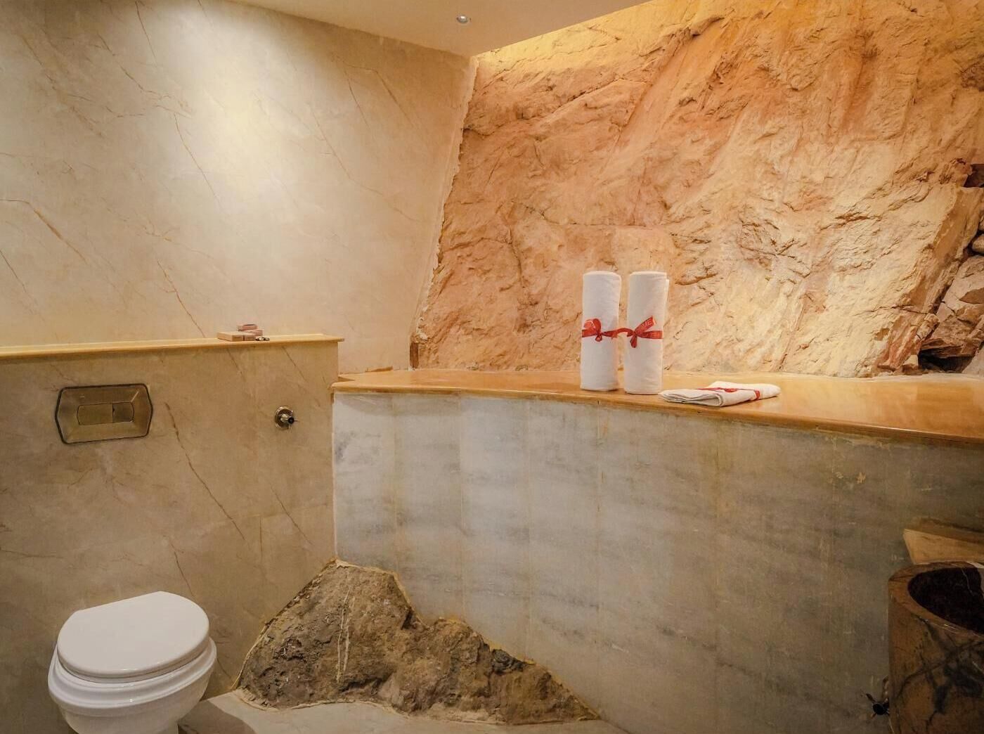 A bathroom with a marble wall, a toilet, and a sink area with towels.