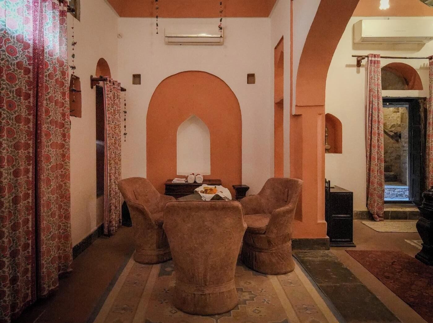 Una habitación con un amplio arco de entrada, una pequeña mesa con sillas y cortinas estampadas.