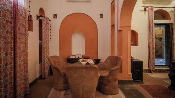 Una habitación con un amplio arco de entrada, una pequeña mesa con sillas y cortinas estampadas.