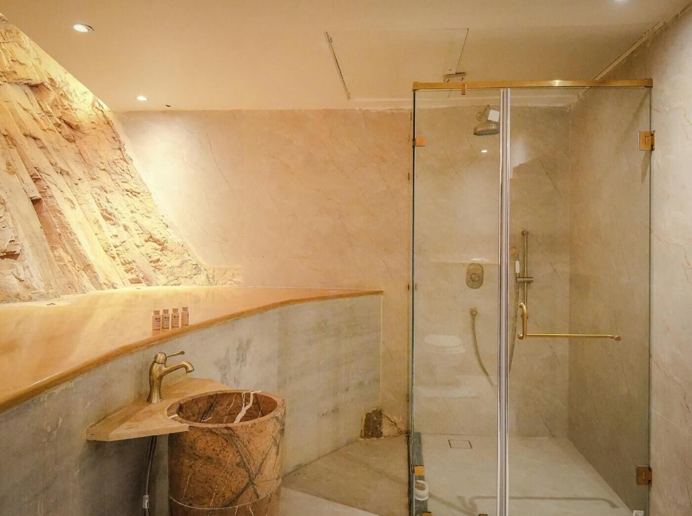Un baño moderno con cabina de ducha de vidrio, encimera de mármol y pared de piedra.