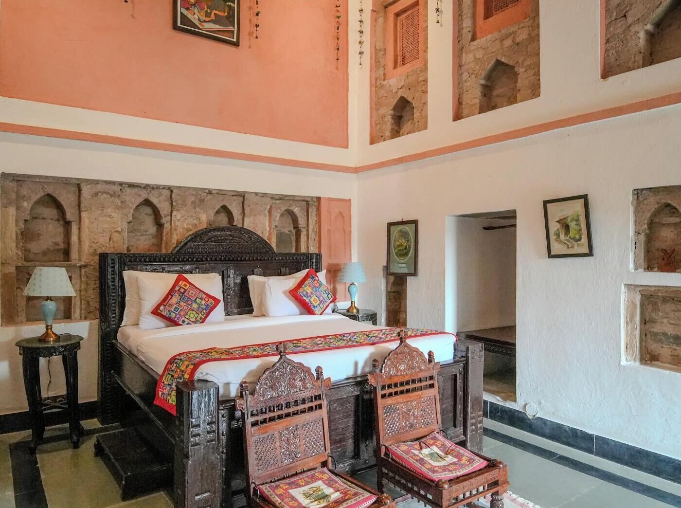 A traditional room with a bed, two chairs, a nightstand, and a wall with decorative elements.