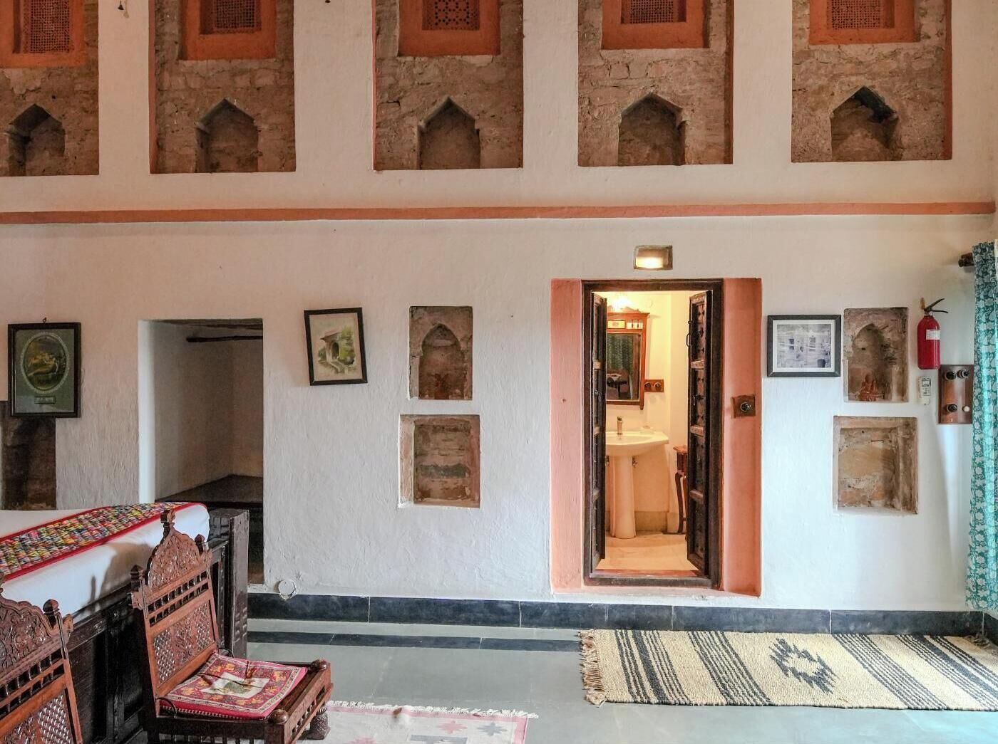 Una habitación con techo alto, un acceso a baño y un tapete estampado en el suelo.