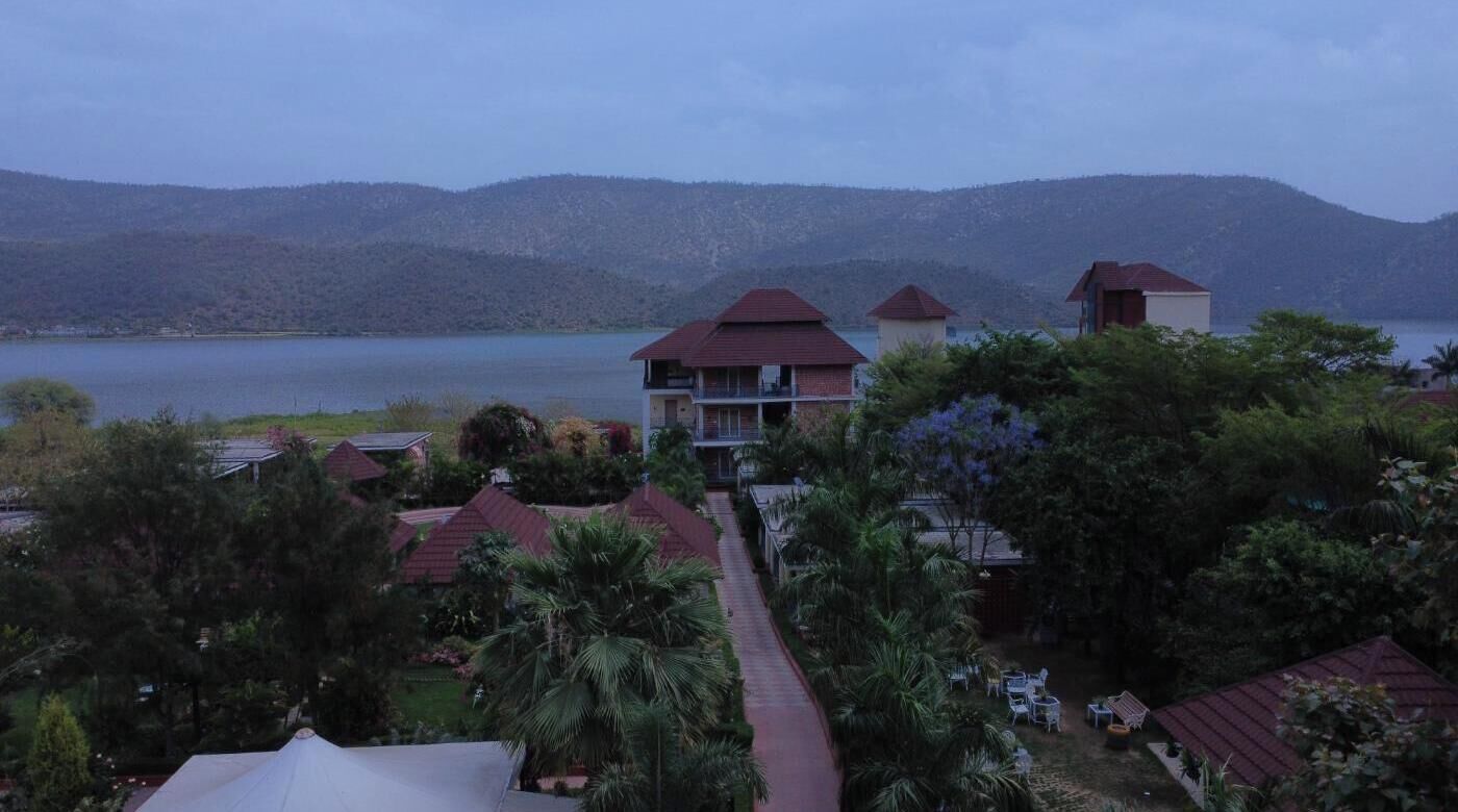 Een resort met meerdere gebouwen, een pad en een meer met bergen op de achtergrond.