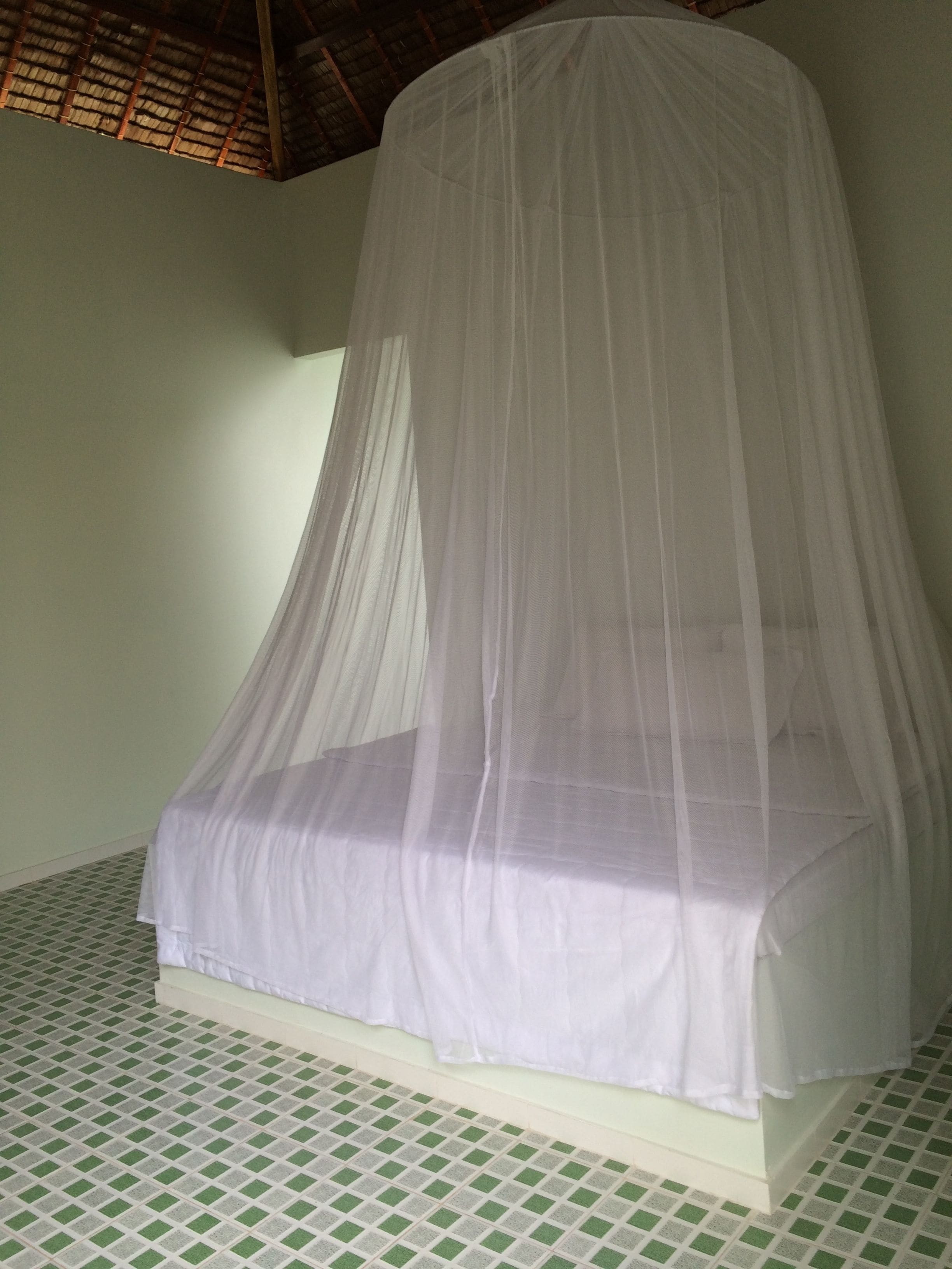 Una cama con dosel blanco en una habitación con piso blanco y verde a cuadros y una pared blanca lisa.
