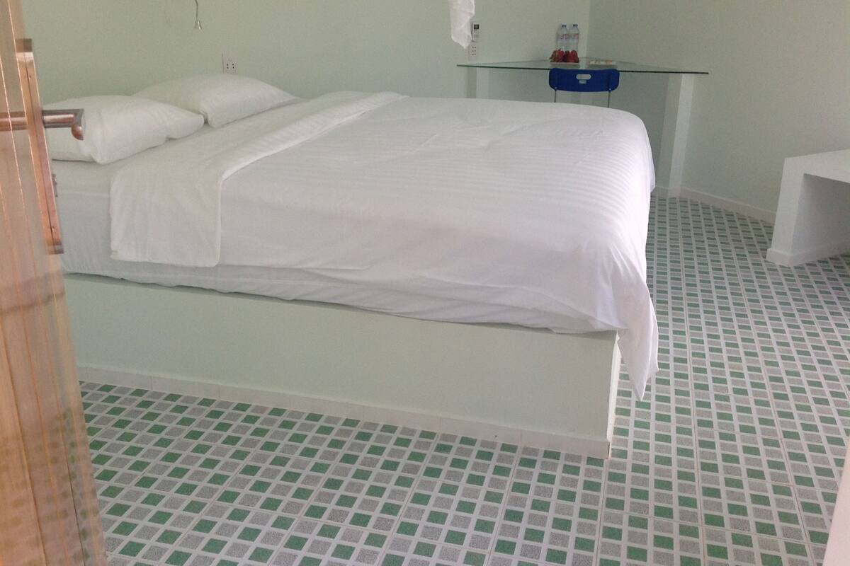 A hotel room with a bed, a small table with water bottles, and a chair.