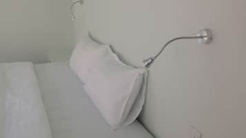 A bed with white bedding and a white pillow, a wall-mounted light fixture, and a power outlet.