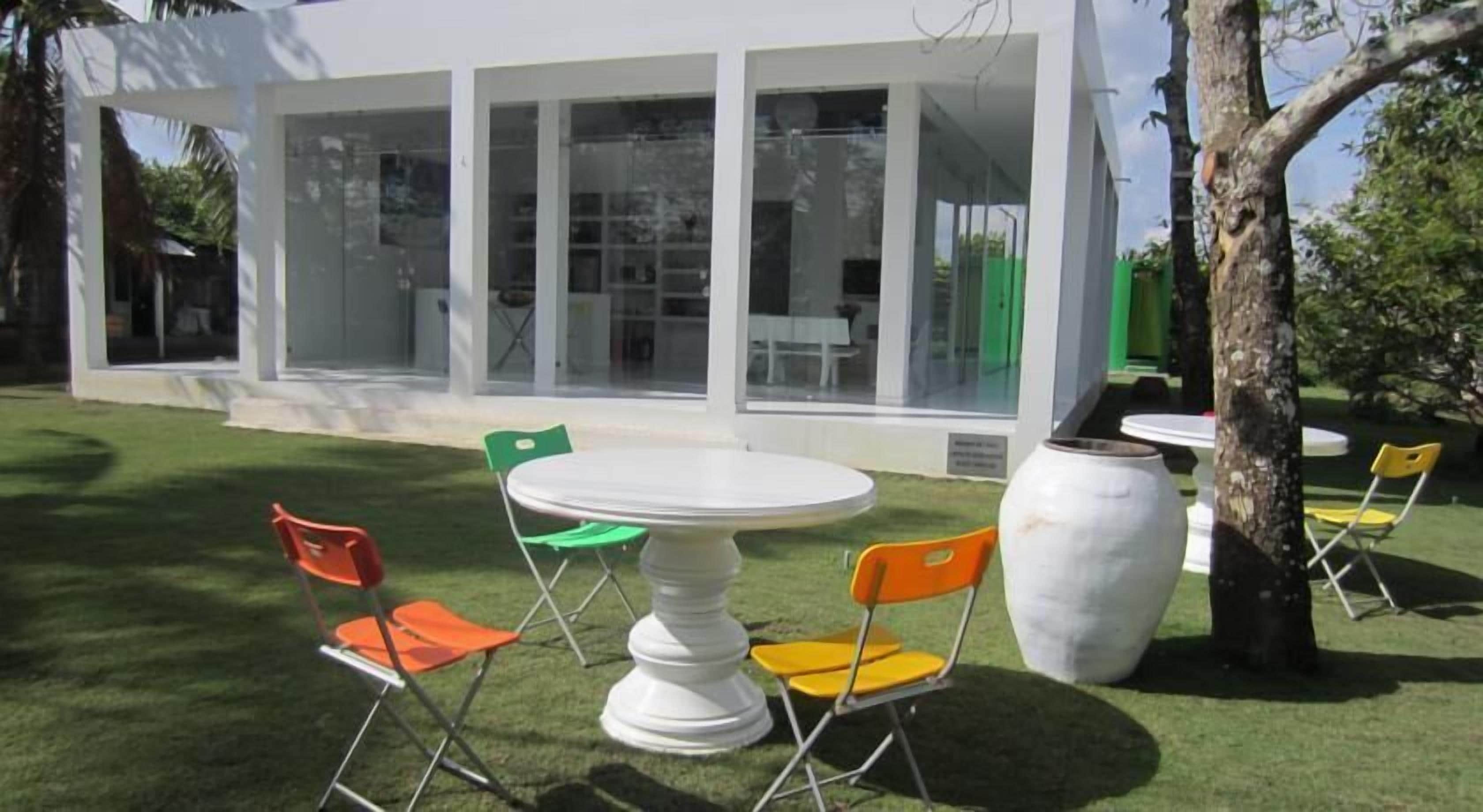 A modern outdoor seating area with a white table and chairs, a large vase, and a tree.