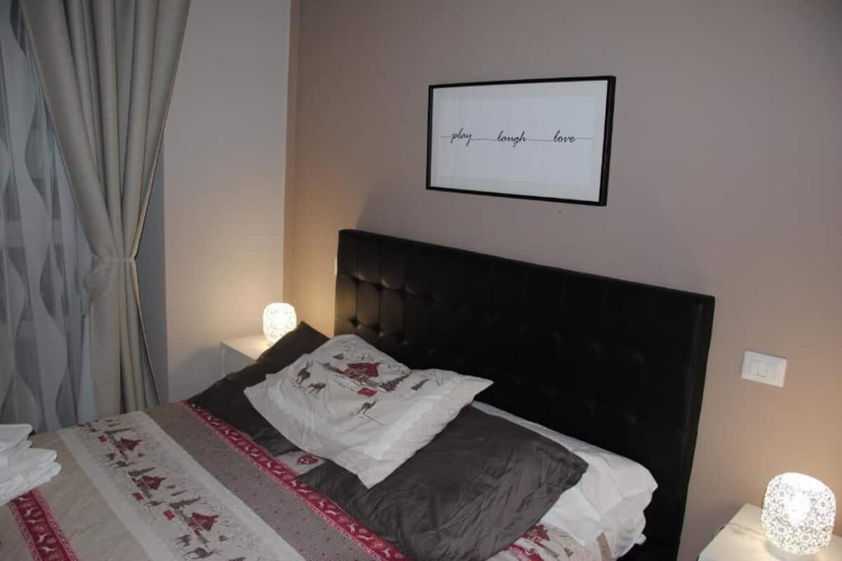 A neatly made bed with a patterned bedspread, a framed inspirational quote on the wall, and a bedside lamp.