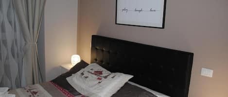 En pænt redt seng med et mønstret dynebetræk, et inspirerende citat i ramme på væggen og en senget lampe.