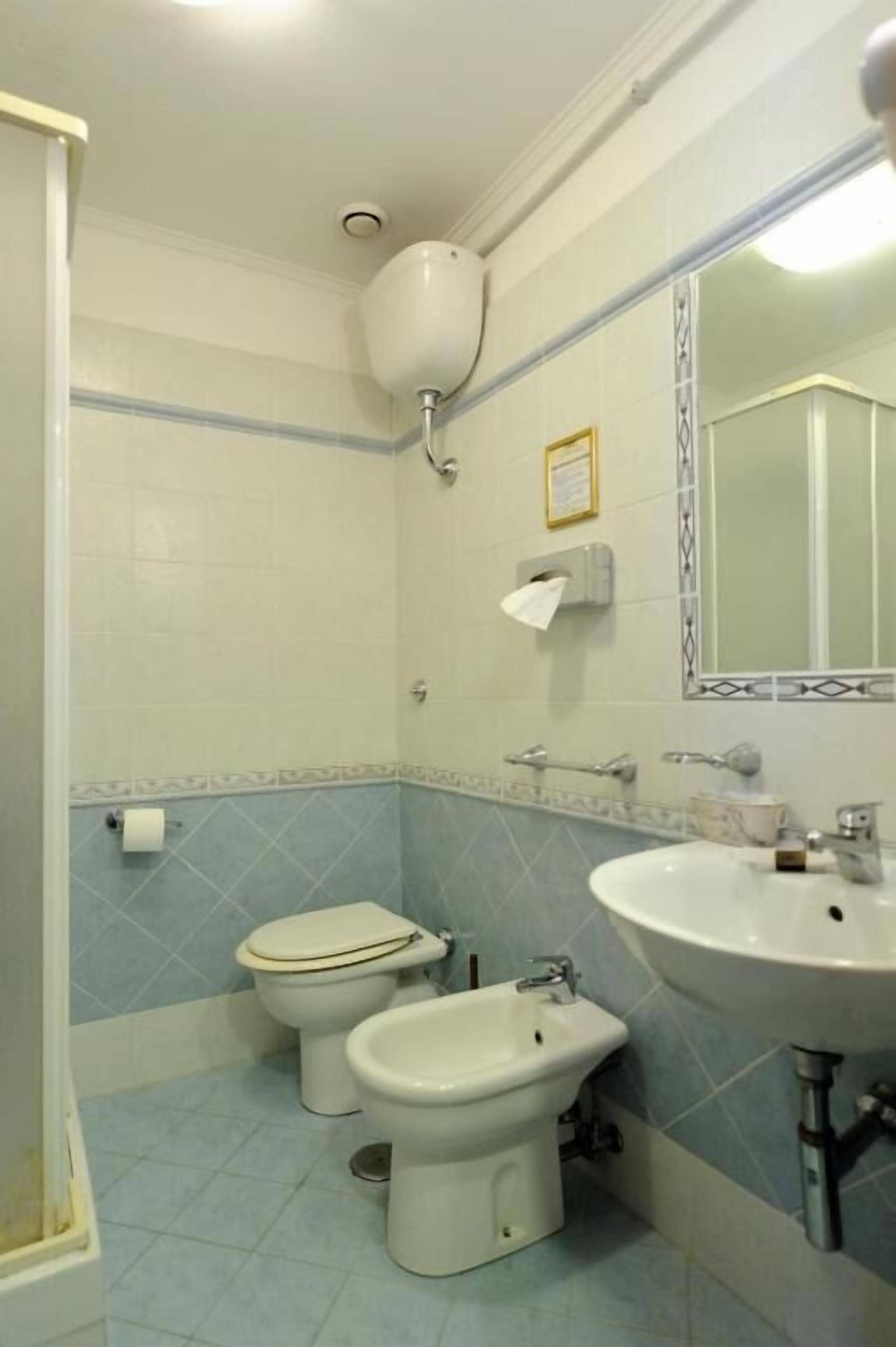 A bathroom with two toilets, a bidet, a sink, and a mirror.