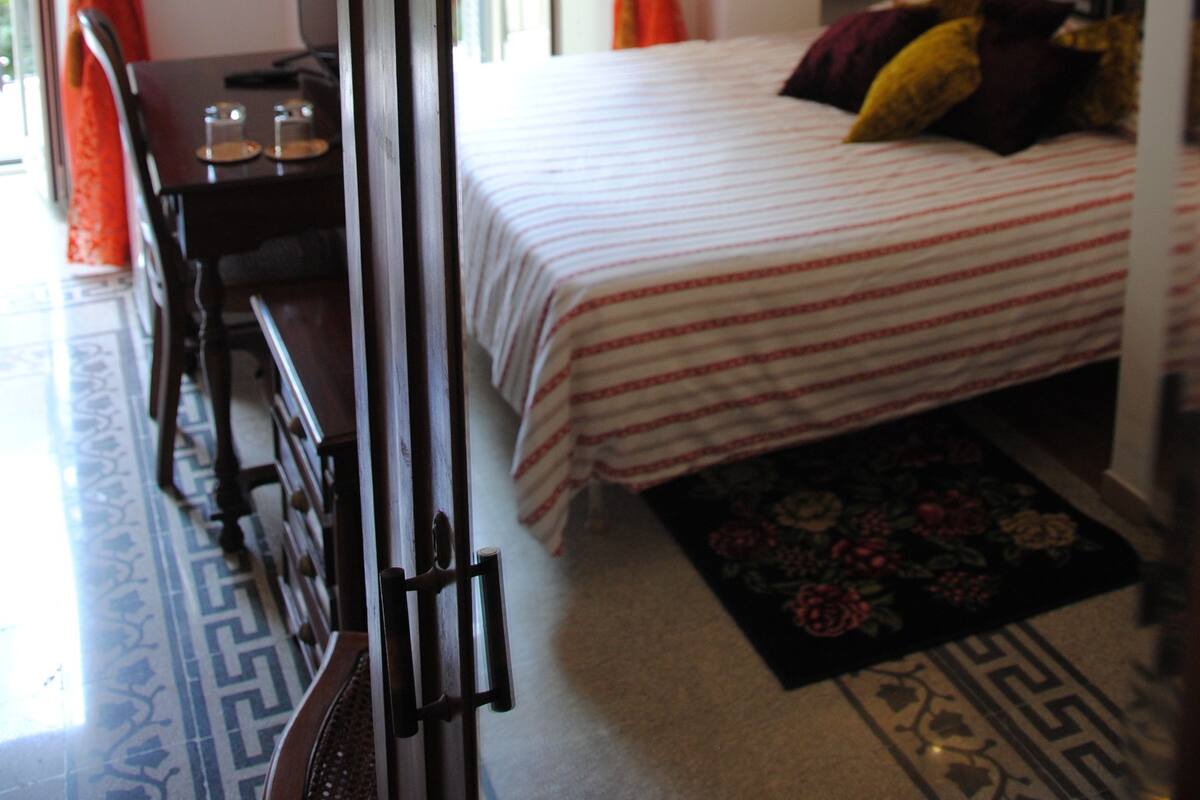A bedroom with a bed, a desk, a chair, and a window with curtains.