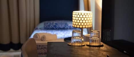 Une table bien rangée, avec une lampe et trois photophores en verre, dans une chambre d’hôtel.