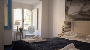 Habitación de hotel con una cama grande, una silla, una mesita con lámpara y vistas al exterior.