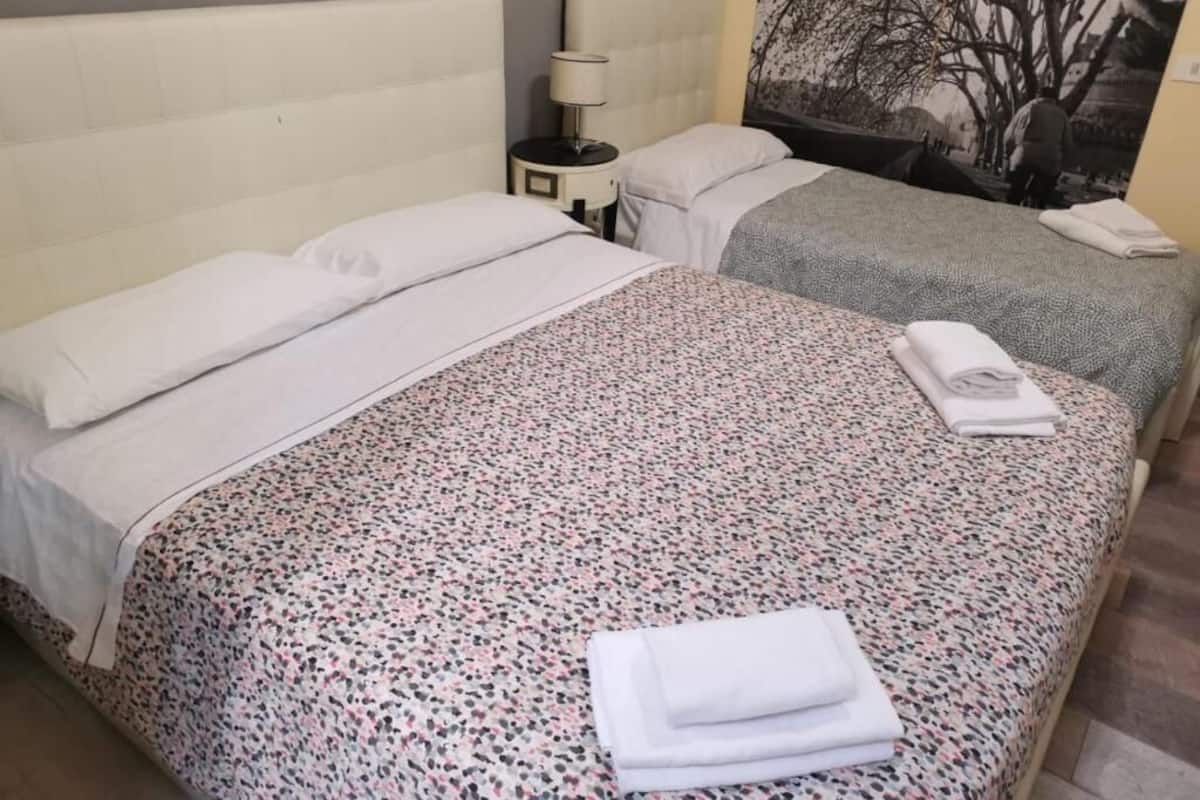 A hotel room with two beds, a nightstand with a lamp, and a wall-mounted artwork.