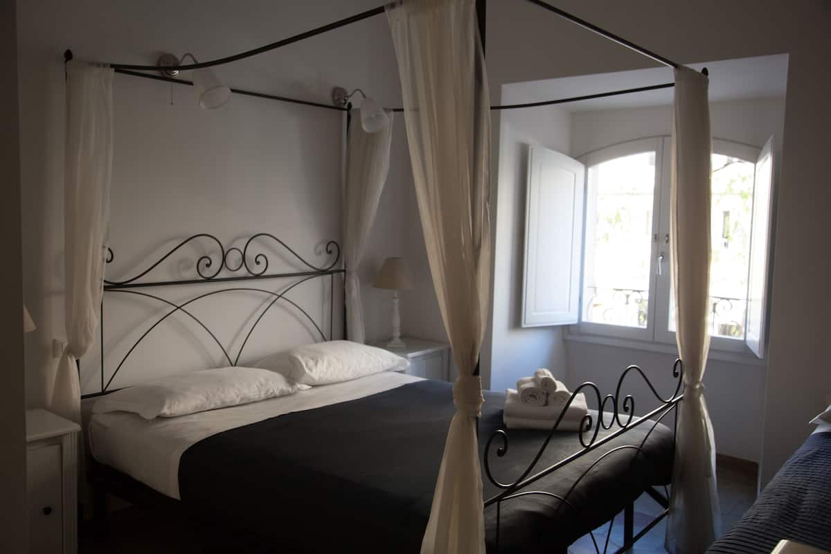 A four-poster bed with a canopy, a bedside table with a lamp, and a window with curtains.