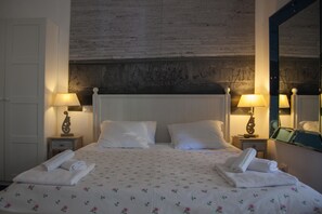 Un letto rifatto con biancheria a fiori, due comodini con lampade e un grande specchio a parete.