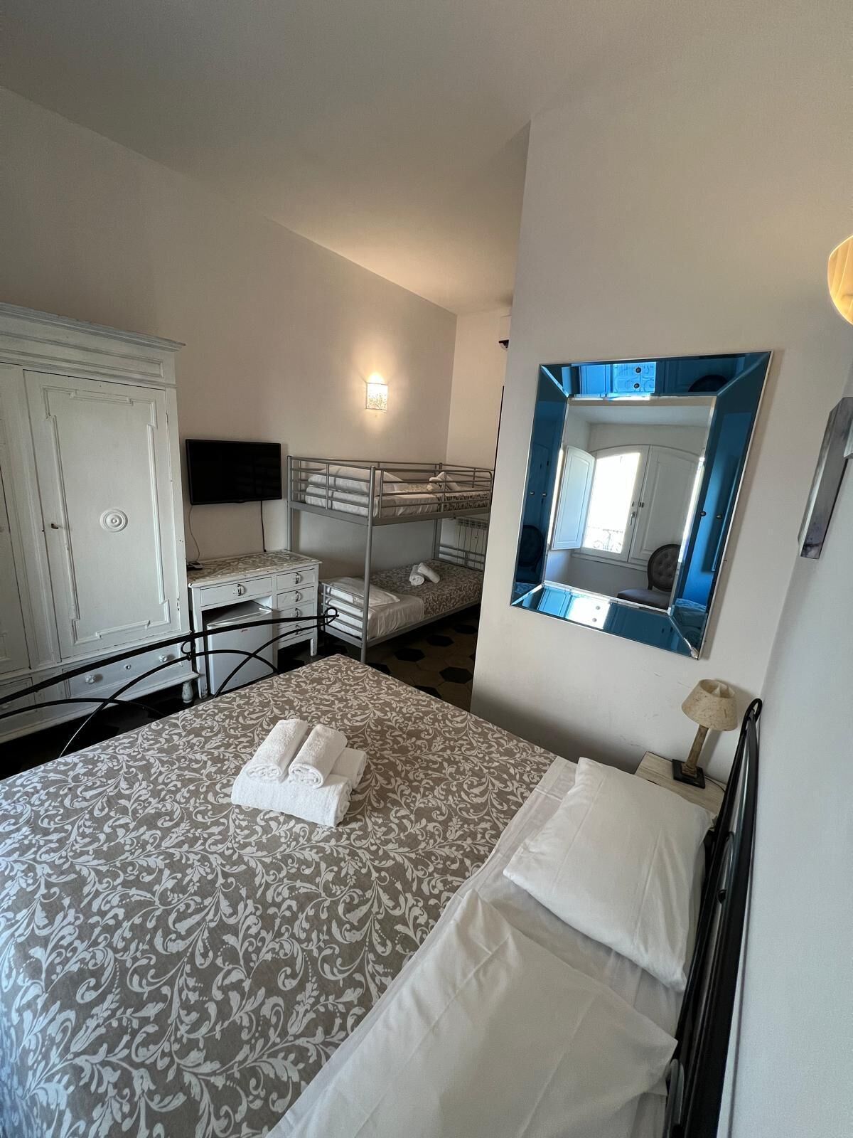 A hotel room with a large bed, a wardrobe, a desk, and a mirror.