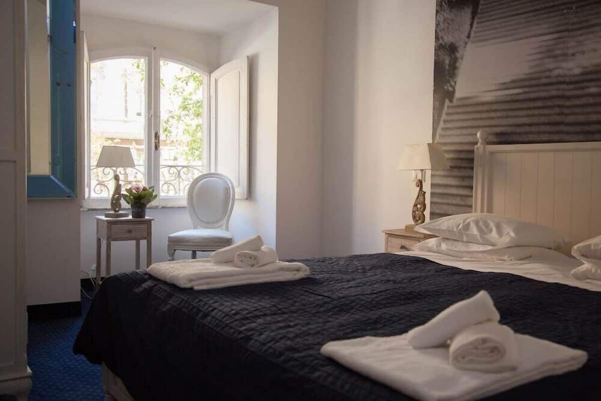 A hotel room with a bed, a chair, a nightstand, and a window with a view of the outside.