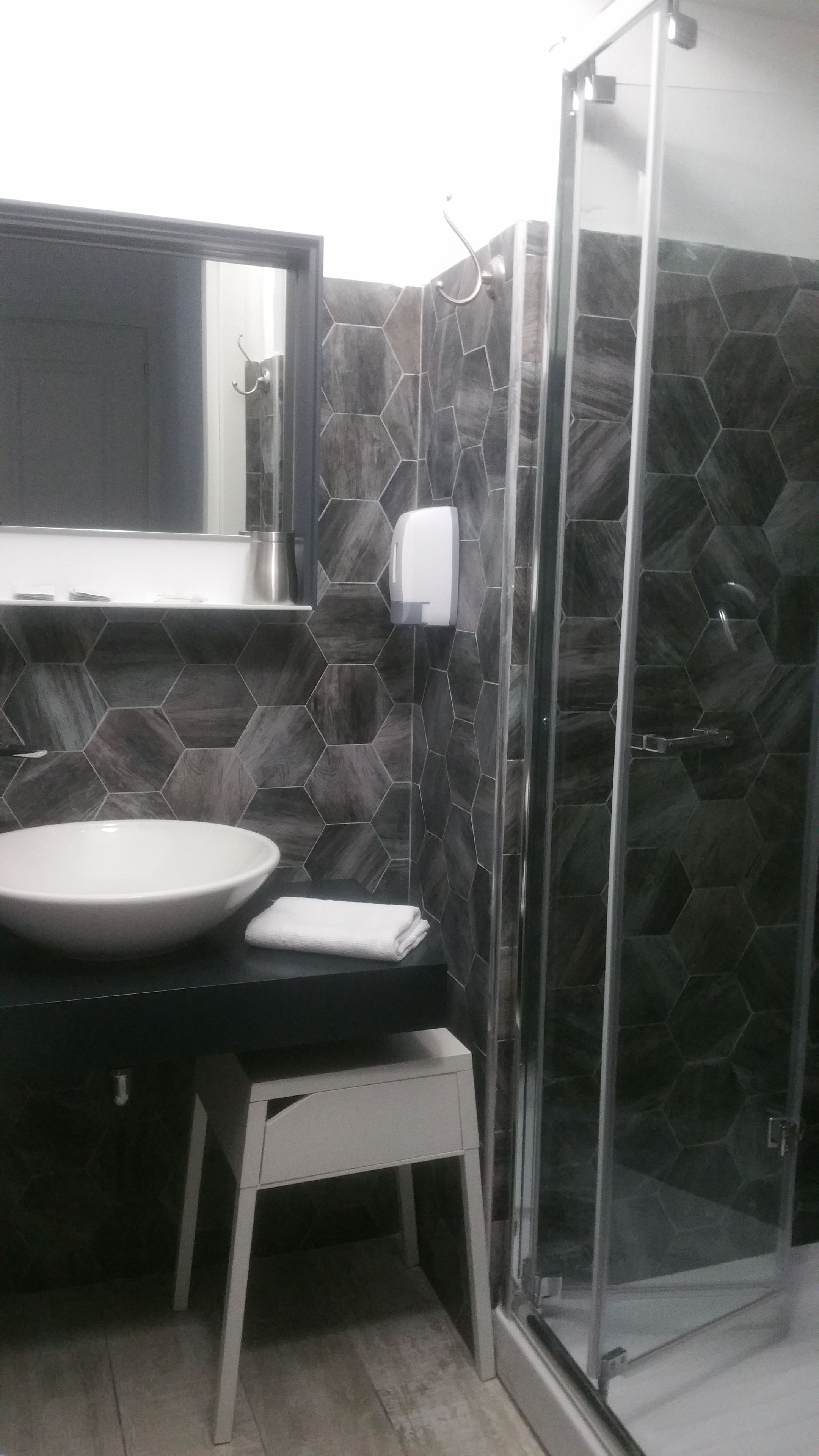Een badkamer met een wand betegeld met hexagontegels, een wit wastafelmeubel, een spiegel boven de wastafel en een douchecabine met glazen wanden.
