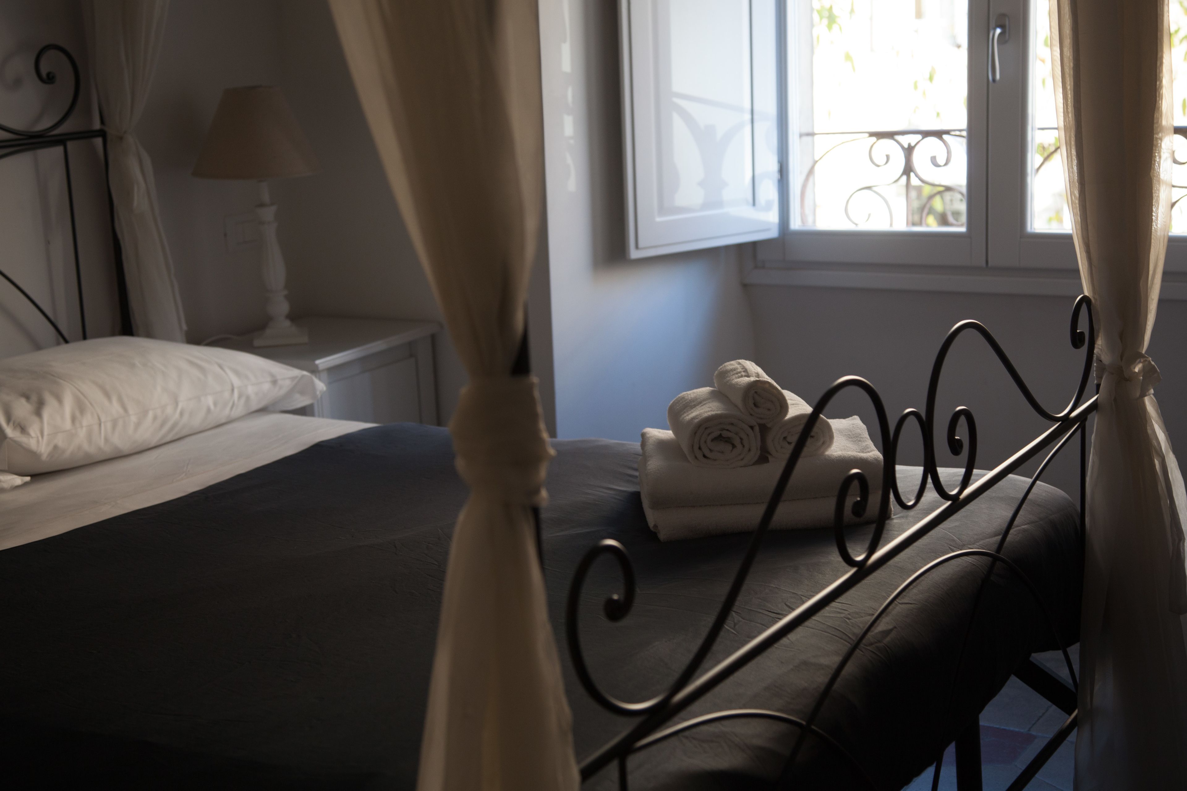 A bedroom with a bed, a nightstand, a lamp, a window with curtains, and a view of the outside balcony.