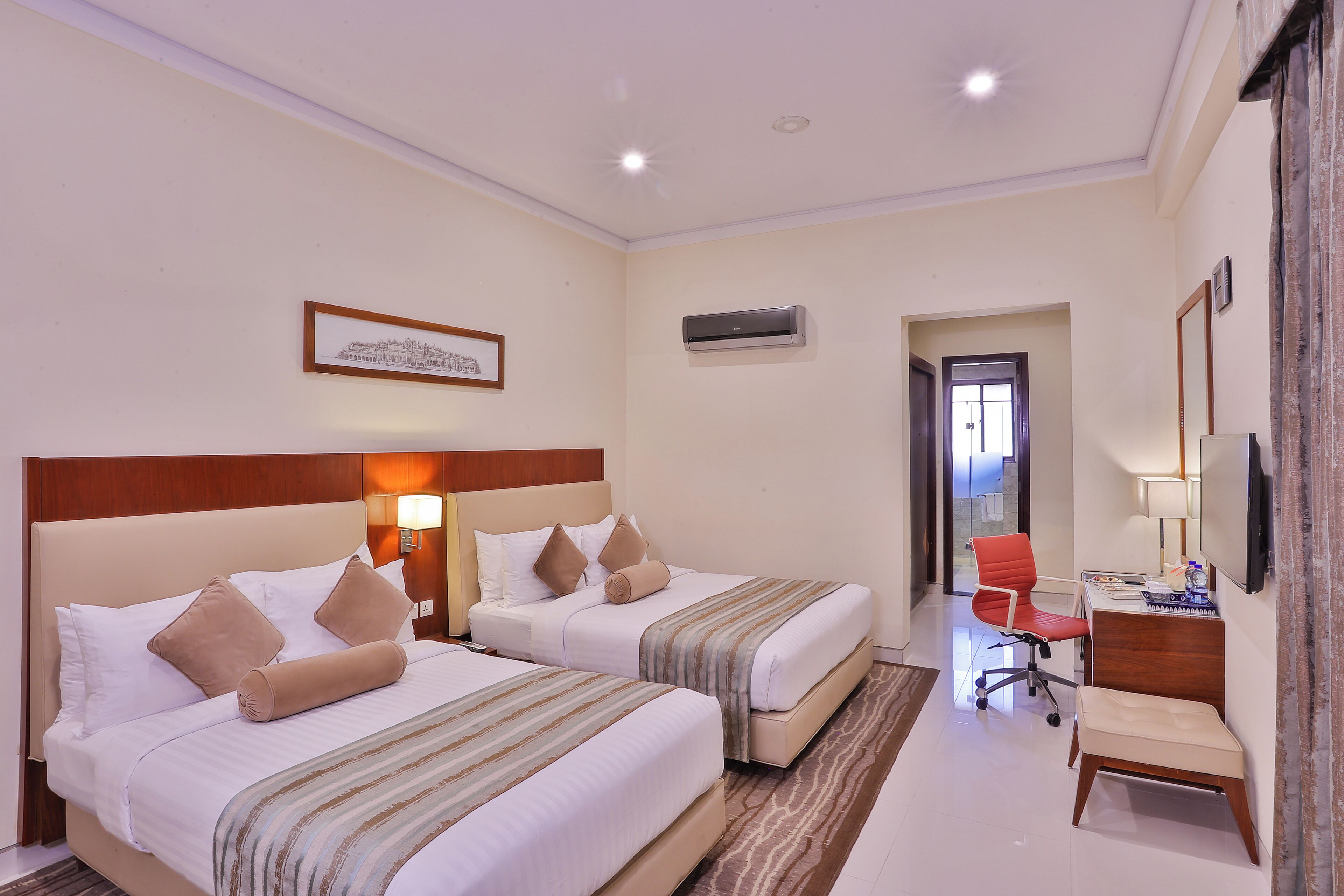 A hotel room with two beds, a desk, a chair, and an air conditioning unit.
