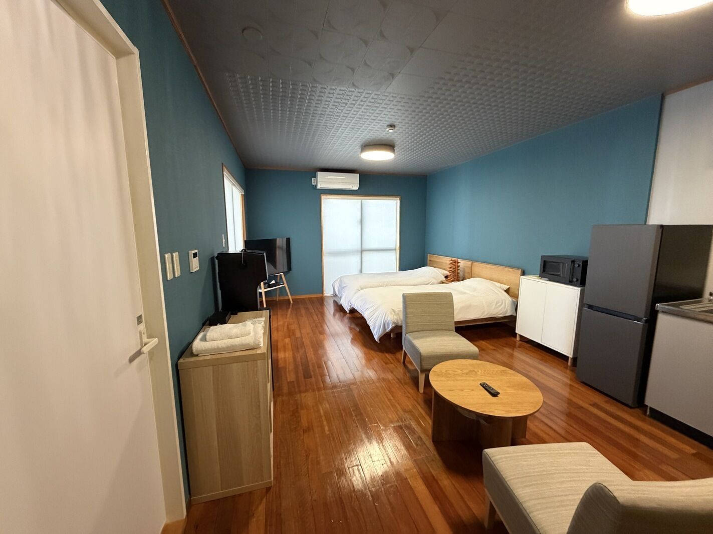 Une chambre d’hôtel équipée d’un lit, d’une télévision, d’un réfrigérateur, d’un four à micro-ondes, d’un plancher en bois et d’une fenêtre.