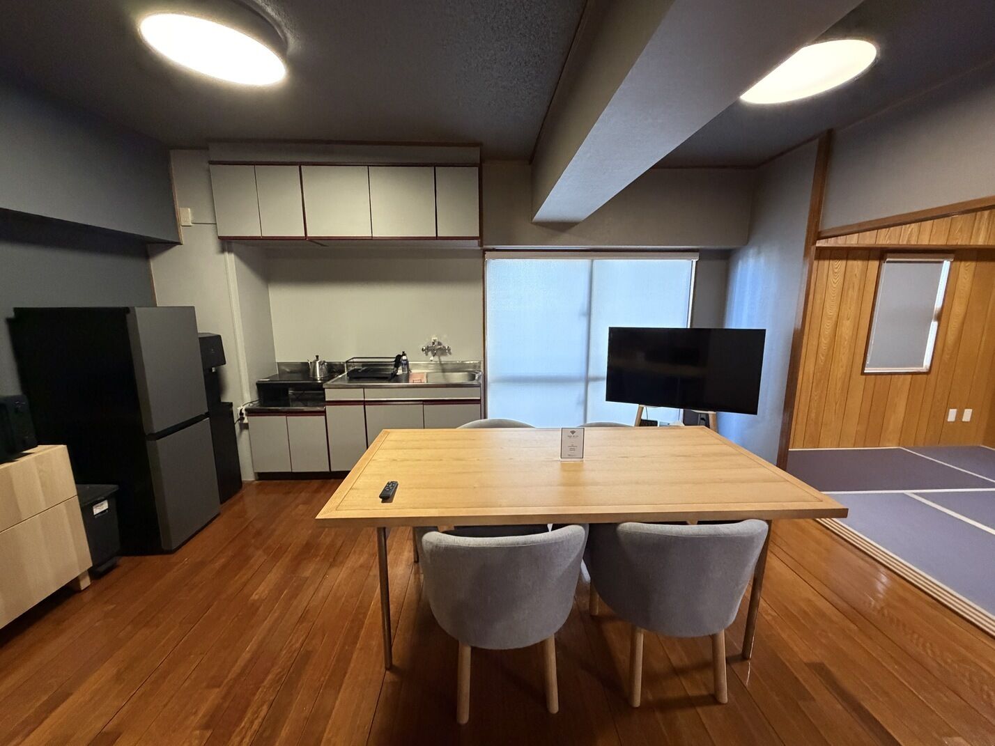Une cuisine moderne équipée d’une table à manger, de chaises, d’un réfrigérateur, d’un évier et d’un téléviseur.